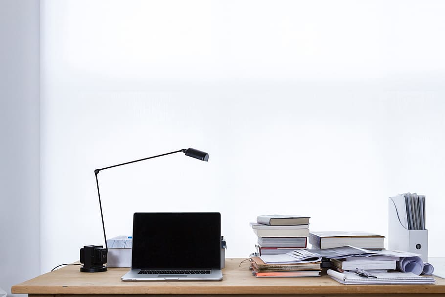 MacBook Pro beside pile of assorted-color labeled books on brown wooden desk HD wallpaper