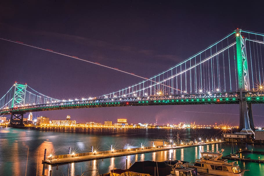 suspension bridge with string lights at nighttime, green lighted bridge above body of water HD wallpaper