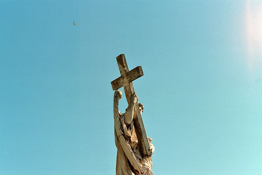 blue skies, worm's eye view of man holding cross statue during daytime HD wallpaper