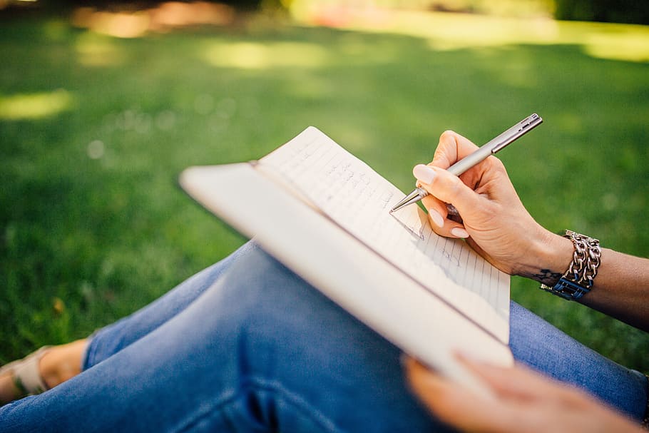 person writing on notepad sitting on green grass in selective focus photography at daytime, HD wallpaper