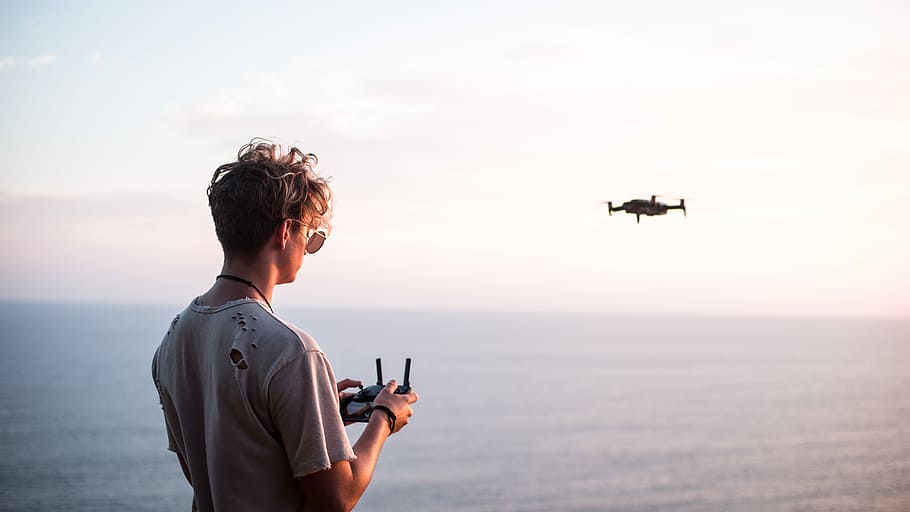 man using quadcopter drone near sea during daytime, man controlling quadcopter drone above the sea during daytime HD wallpaper