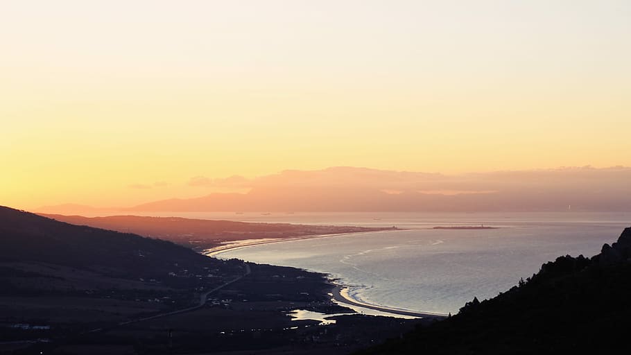 body of water beside mountains, silhouette of mountain near ocean during golden hour HD wallpaper