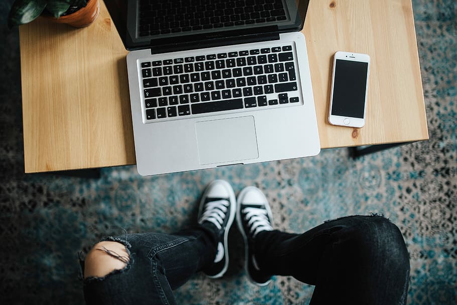 Woman in ripped jeans and black sneakers with a silver laptop on a wooden table HD wallpaper