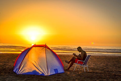 man sitting on chair playing guitar  near tent on beach shore during sunset HD wallpaper