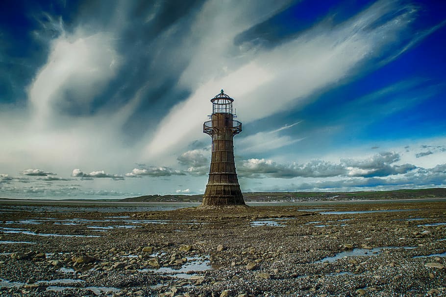 time lapse photography of brown lighthouse underneath blue cloudy skies HD wallpaper