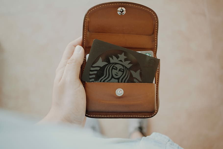 green Starbucks gift card inside brown leather wallet, person holding brown leather wallet with Starbucks card