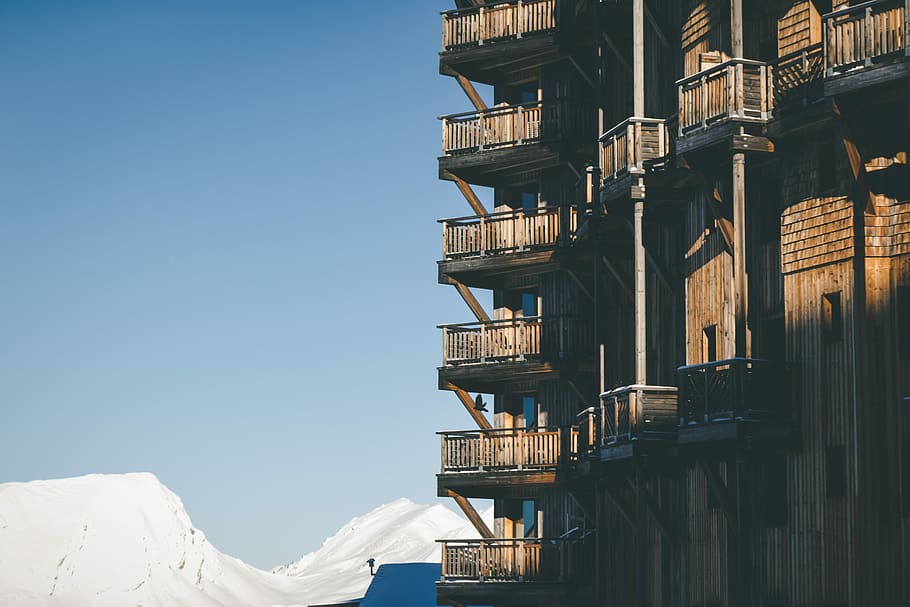 selective photography of brown and black building under blue sky at daytime, high rise concrete building near white snow mountain at daytime HD wallpaper