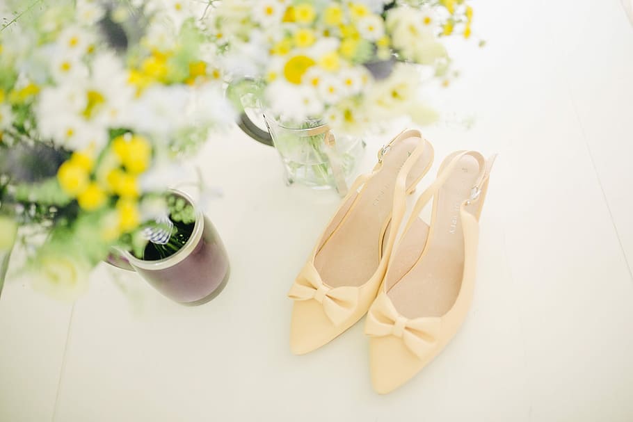 pair of women's beige pointed-toe slingback pumps with ribbons near flower vase, pair of yellow slingback strap stilettos