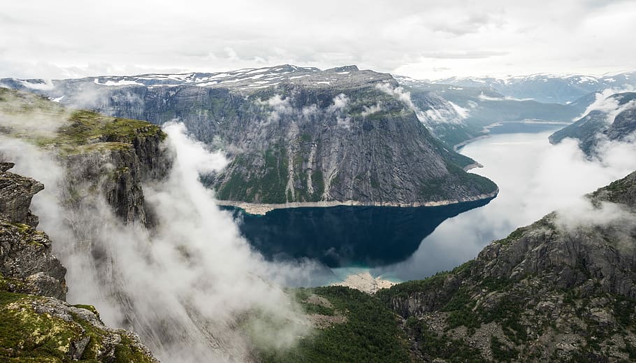 photo of misty mountain, body of water in the middle of mountain during daytime HD wallpaper