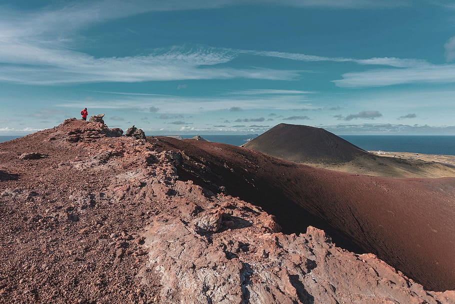 photo of person standing at peaked of mountain, red rocky mountain HD wallpaper