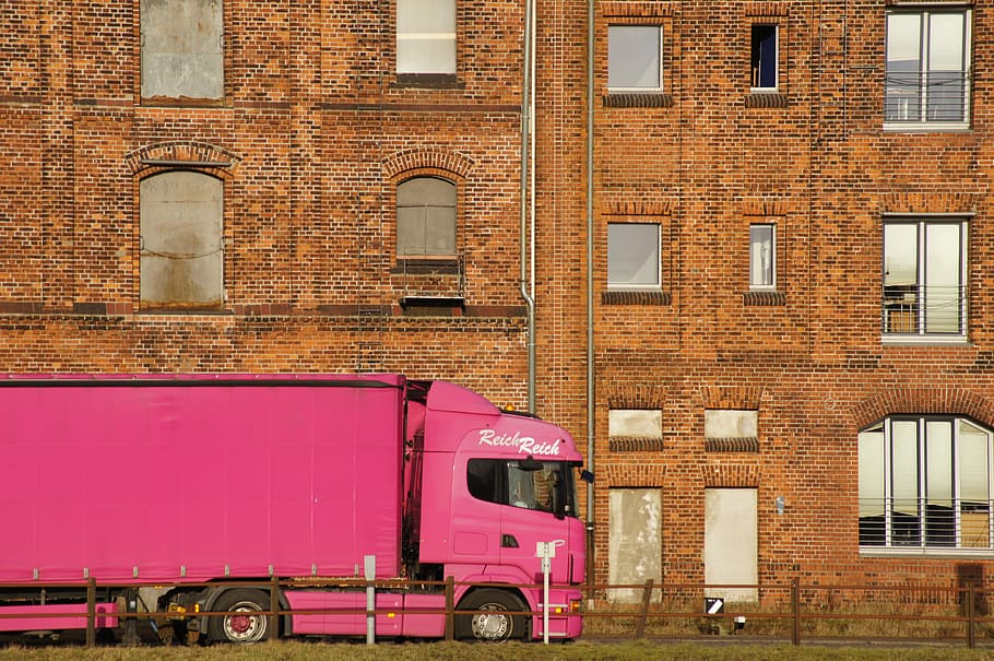 pink freight truck near brown concrete building during daytime HD wallpaper