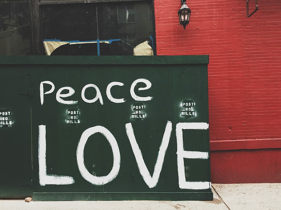 Peace Love painted on green wall, person taking photo of peace love signage leaning on concrete wall during daytime HD wallpaper
