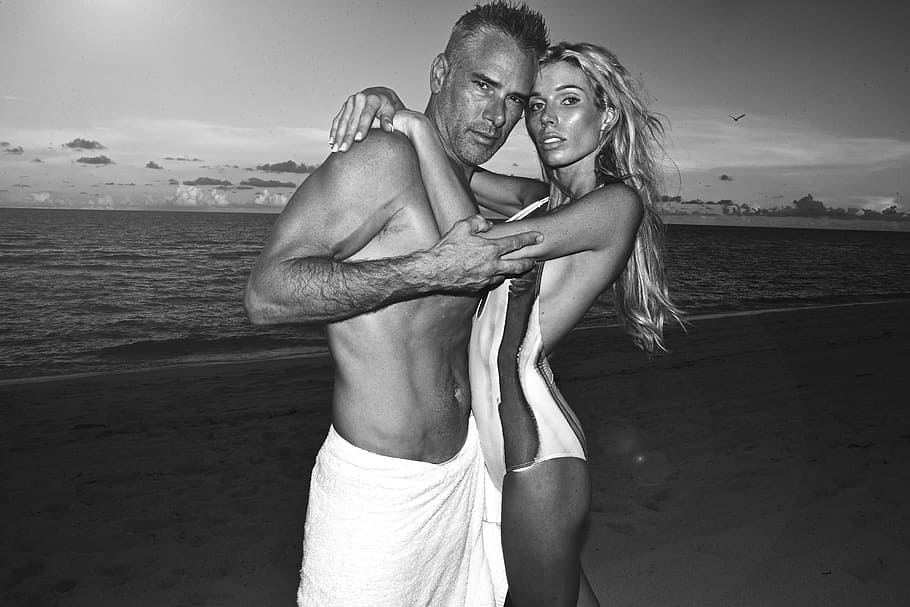grayscale photography of man and woman standing near body of water HD wallpaper