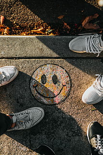 smiley paint on gray ground in front of people, two pairs of gray shoes on gray concrete ground HD wallpaper