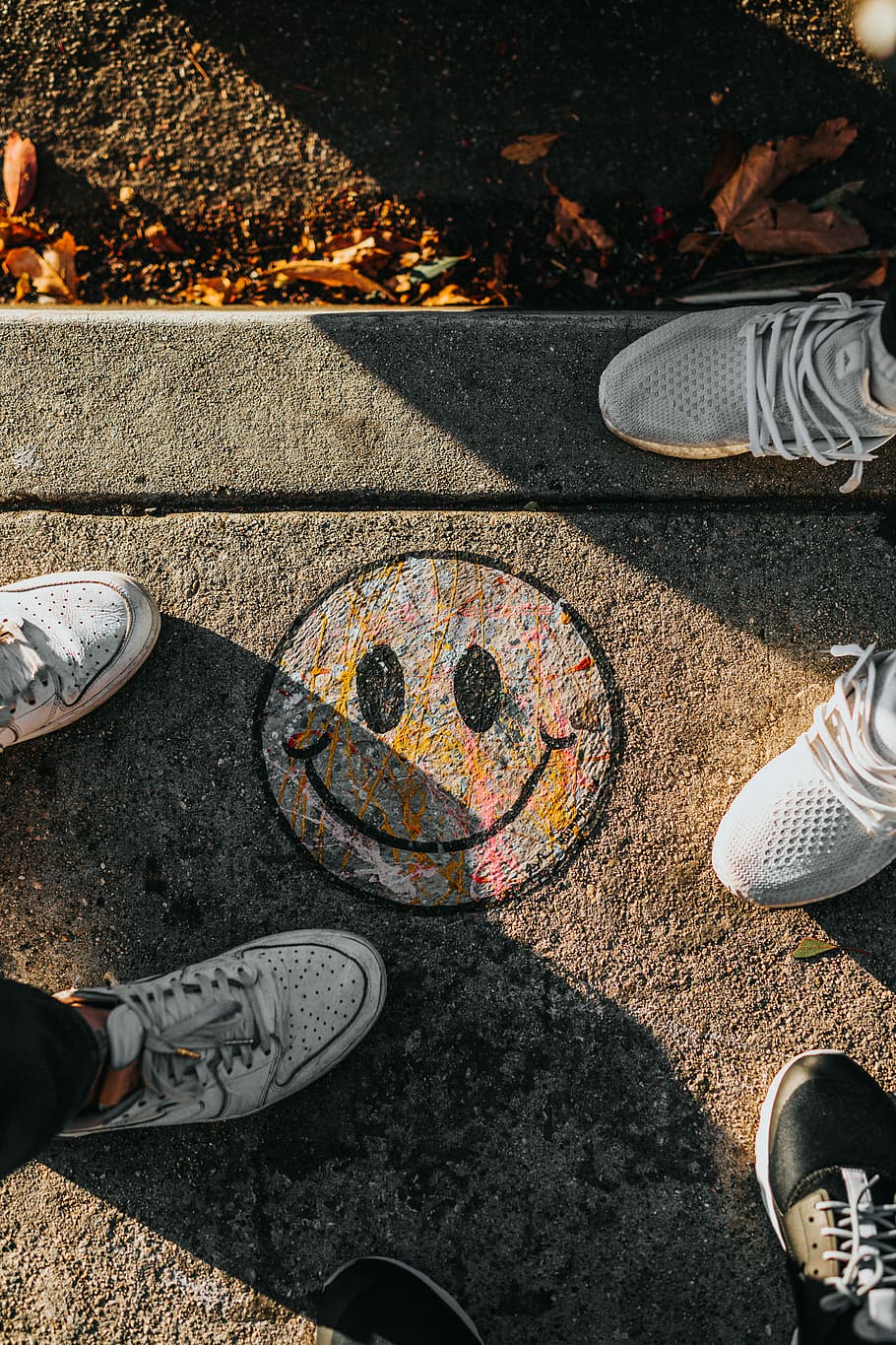 smiley paint on gray ground in front of people, two pairs of gray shoes on gray concrete ground HD wallpaper
