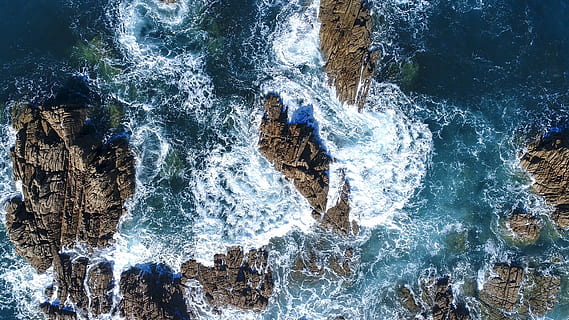 ocean waves hammering stone formation, aerial photography of ocean wave crashing on rock formation at daytime HD wallpaper