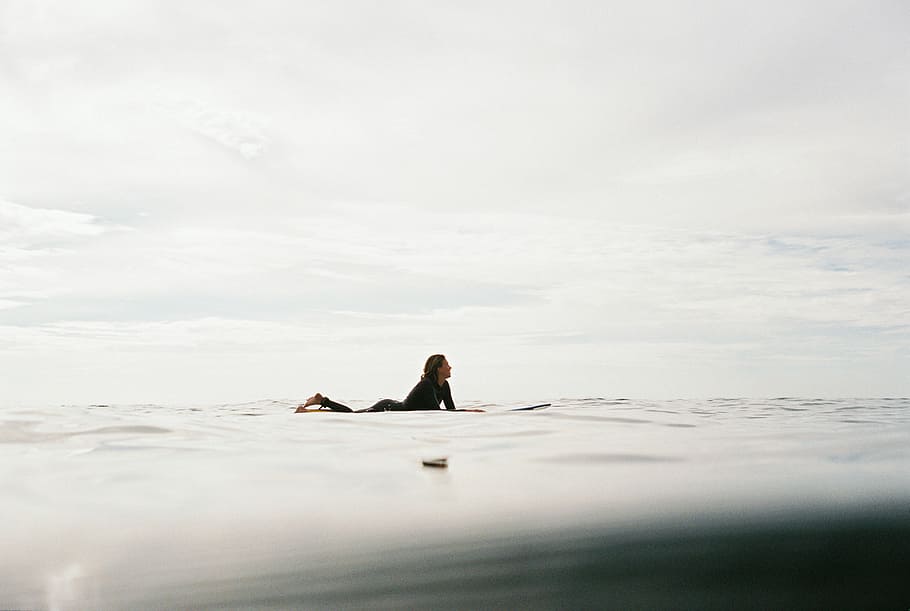 woman lying on surfboard on body of water, woman riding on surfboard during daytime