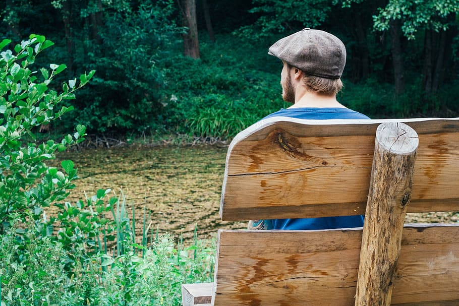 man sitting on the bench near body of water surrounded with trees HD wallpaper