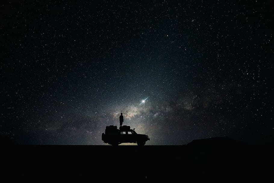 silhouette of off-road car, silhouette photo of person standing on vehicle roof viewing starry sky during nighttime