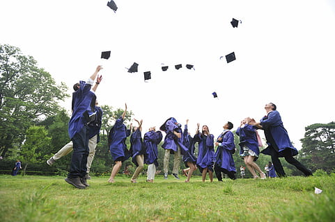 newly graduates on green grass field wearing purple toga throwing their hats on air HD wallpaper