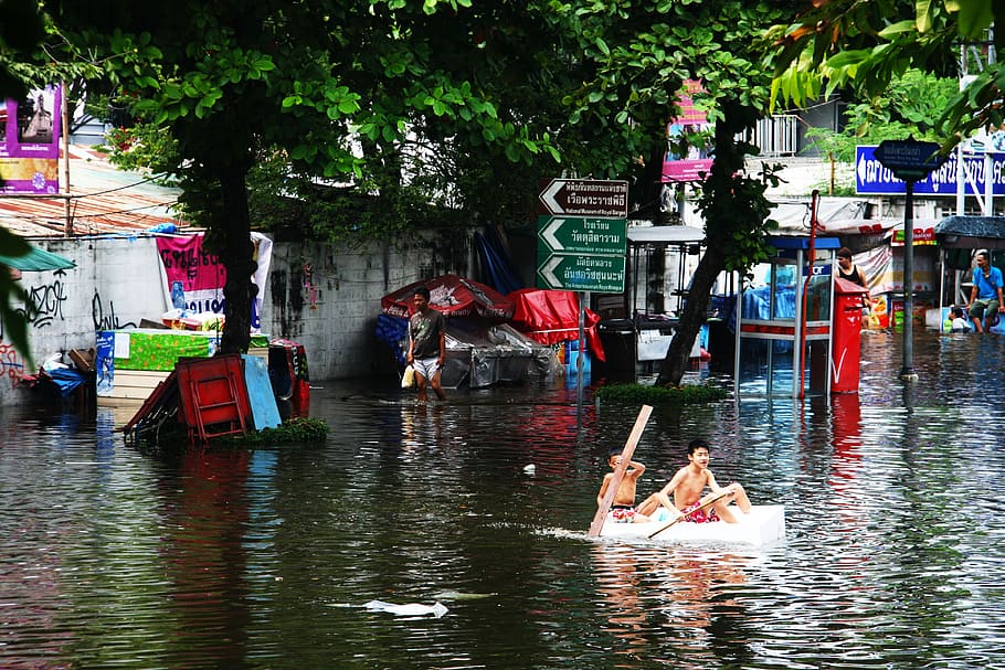two boys riding boat near green trees during daytime, flood, rowing