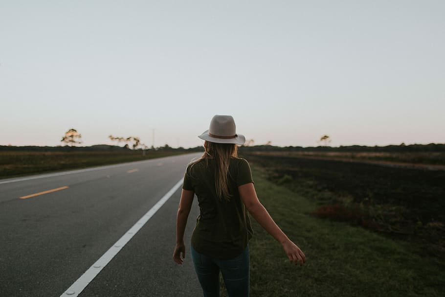 woman walking on side of the road, woman wearing green top and grey hat while walking on grey asphalt road during sunset, HD wallpaper