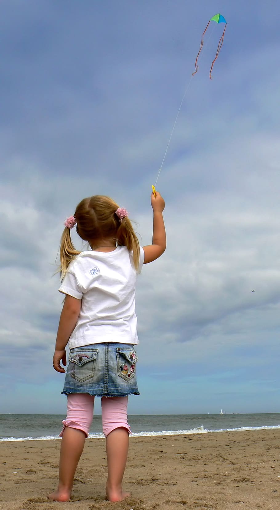 girl holding string of kite flying under white cloudy sky near seashore at daytime HD wallpaper