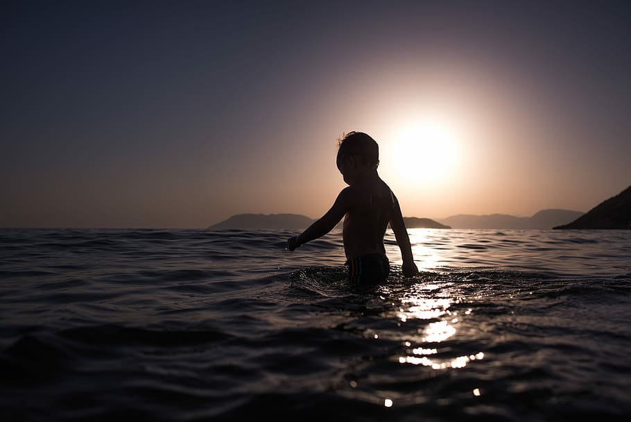 boy standing on body of water, children on sea during dawn, silhouette HD wallpaper