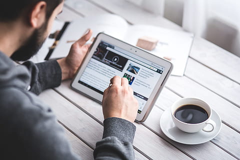 man wearing gray sweater using white tablet computer beside cup filled black coffee HD wallpaper