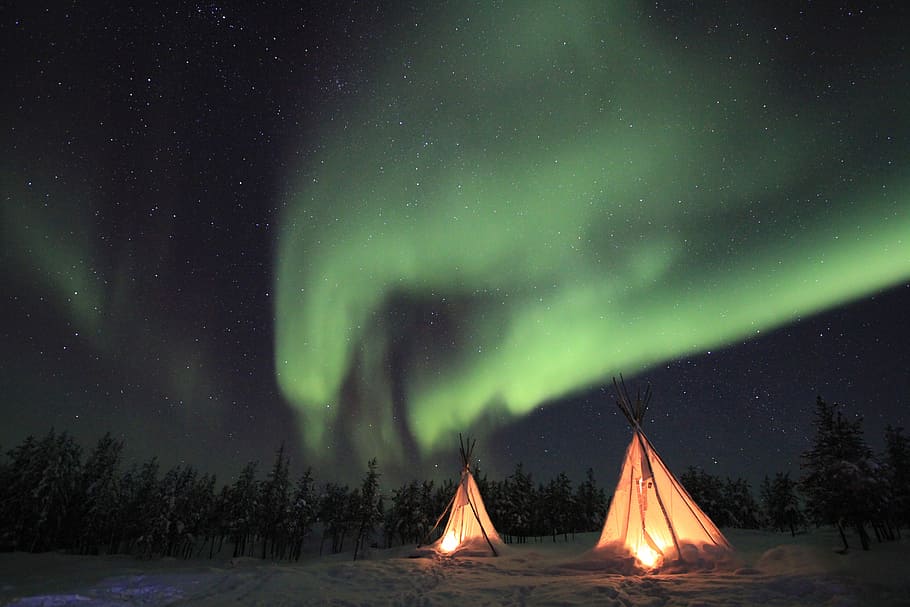 lighted tipi tent under green Northern lights, two white tipi tents under aurora lights