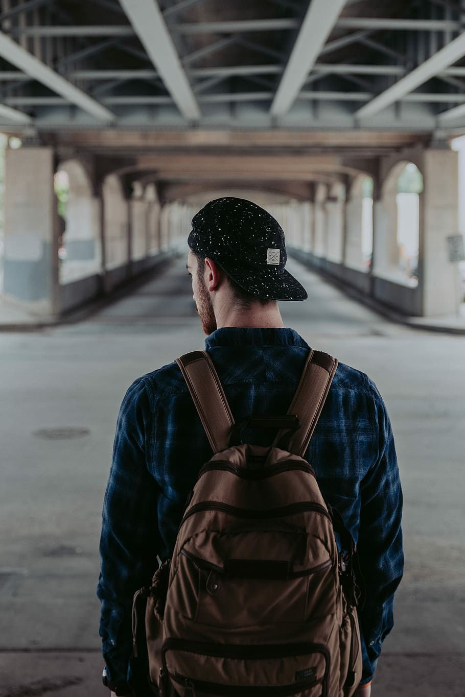 man standing under the bridge, man in blue dress shirt wearing brown backpack HD wallpaper
