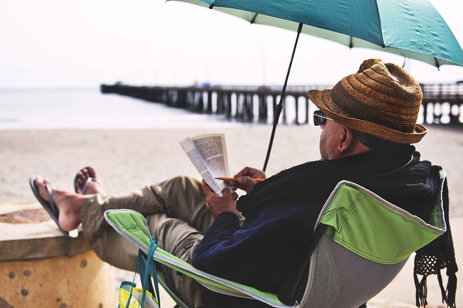 man sitting on chair with green umbrella, person sitting on gray and green camping chair on shore during daytime HD wallpaper
