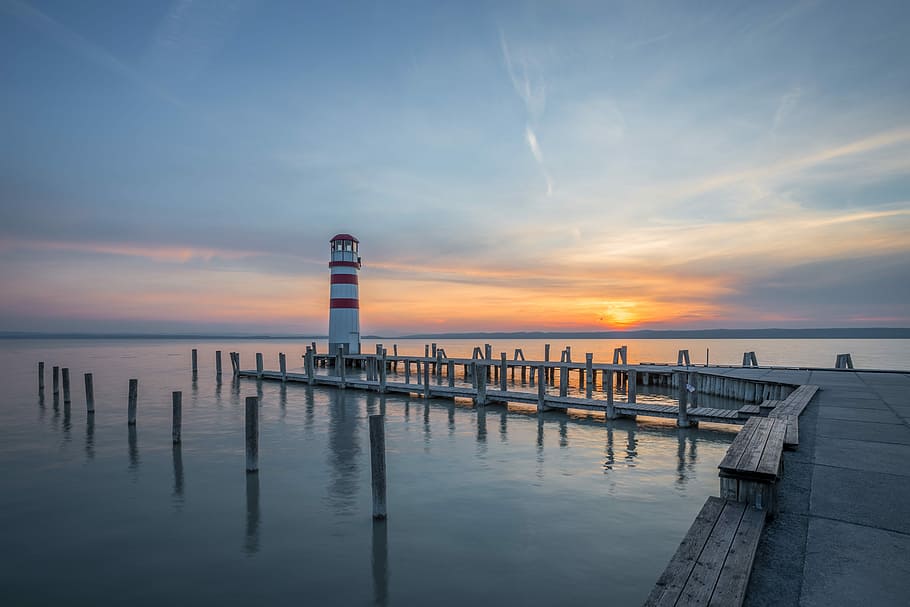 lighthouse at end of docks under clear sky during sunrise, red and white lighthouse during golden hour HD wallpaper