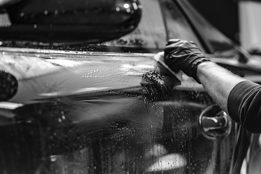 person with gloves holding cloth against car, cleaning, steam