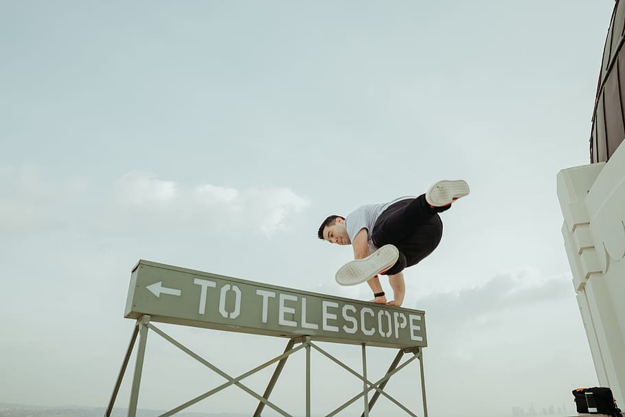 man jumping over to telescope signage, man standing on signage HD wallpaper