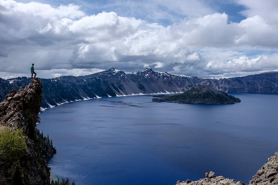 man standing on lake cliff near mountain alps, man standing in top of mountain HD wallpaper