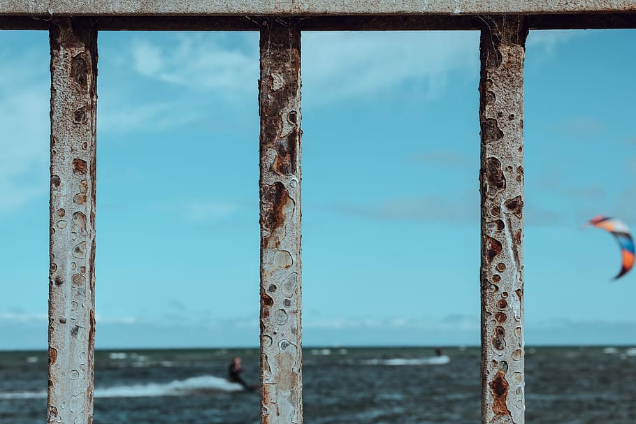 focus photography of rusted fence near beach with surf wind gliding background, gray metal grill HD wallpaper