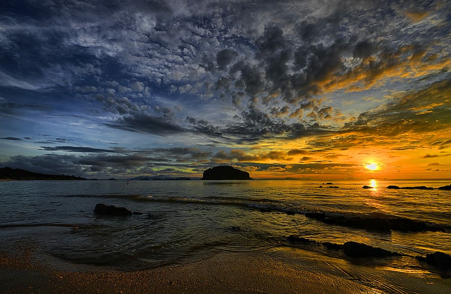 sunset under beach, silhouette of islet on the body of water under blue sky with gray clouds during daytime HD wallpaper