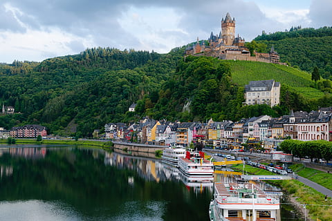brown castle on top of mountain under with multicolored painted buildings near body of water HD wallpaper
