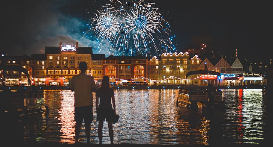 man and woman standing near body of water watching fireworks HD wallpaper