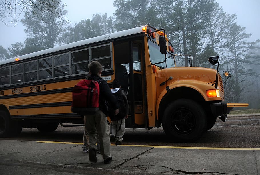 boy carrying black backpack going through yellow school bus, back-to-school