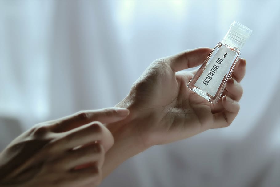 selective focus photography of person's left hand holding clear essential oil bottle HD wallpaper