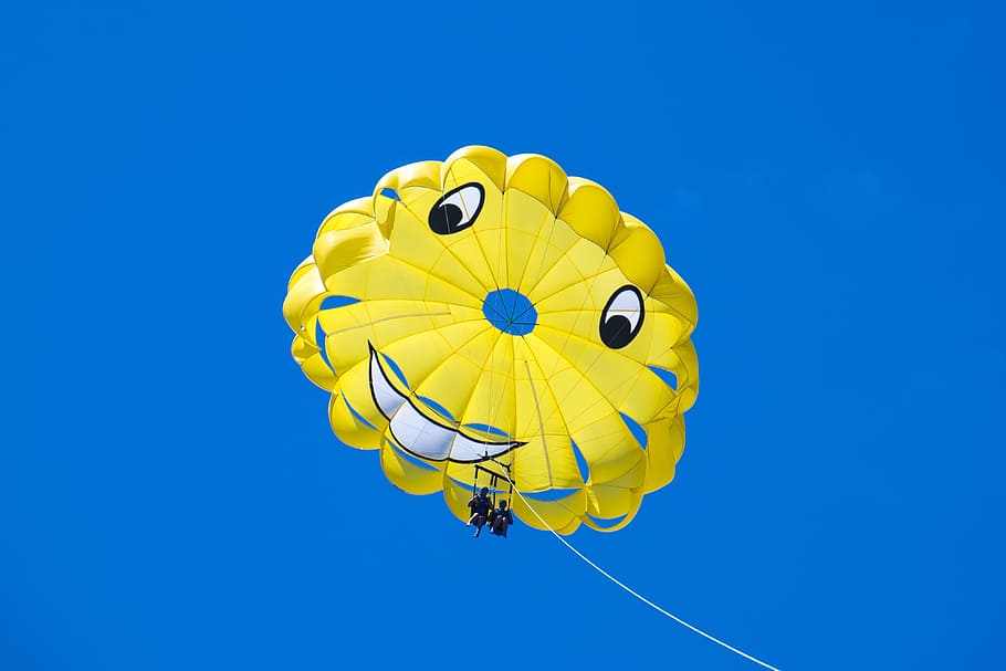 man riding yellow happy face parachute during blue sky, smile