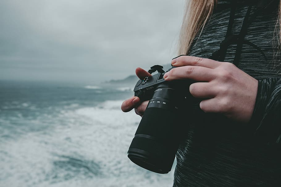 selective focus photography of woman holding camera, person holding black DSLR camera HD wallpaper