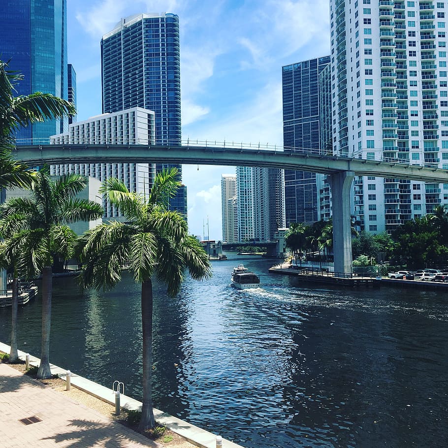 boat under concrete bridge and buildings in distance, Miami, River