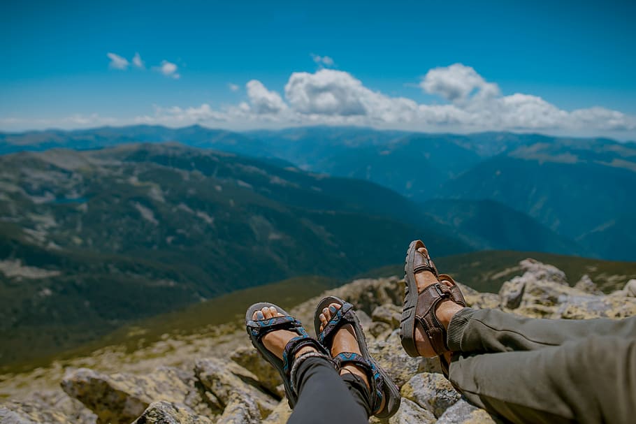 two person's feet cross leg on gray rocks, two person sitting on mountain cliff HD wallpaper