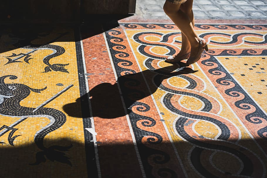 person standing on orange, yellow, and black tiled surface, person walking on brown and black pavement