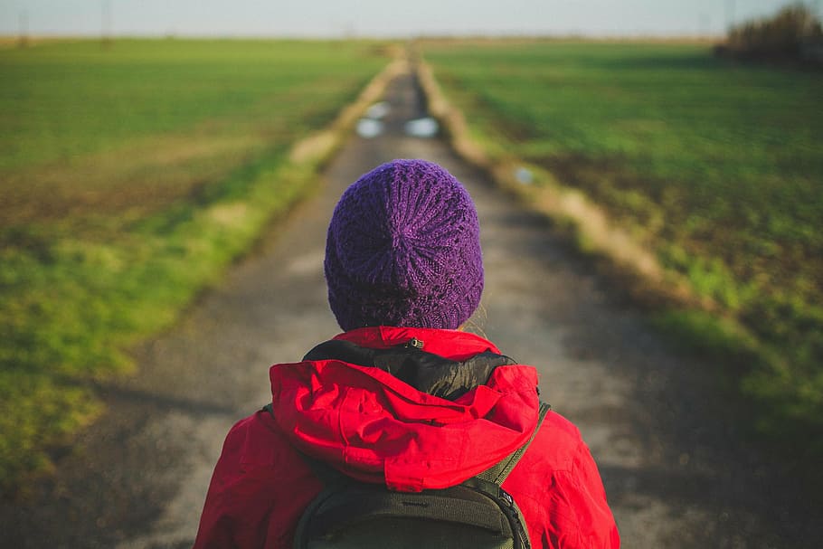person wearing purple knit cap and red hooded jacket facing concrete road between green grass field during daytime