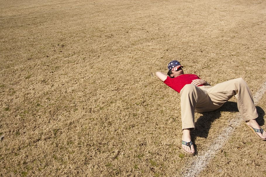 man wearing red t-shirt and brown pants lying on brown grass field HD wallpaper