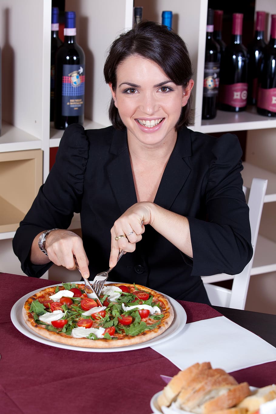 woman in black blazer seating on white chair beside pizza, restaurant